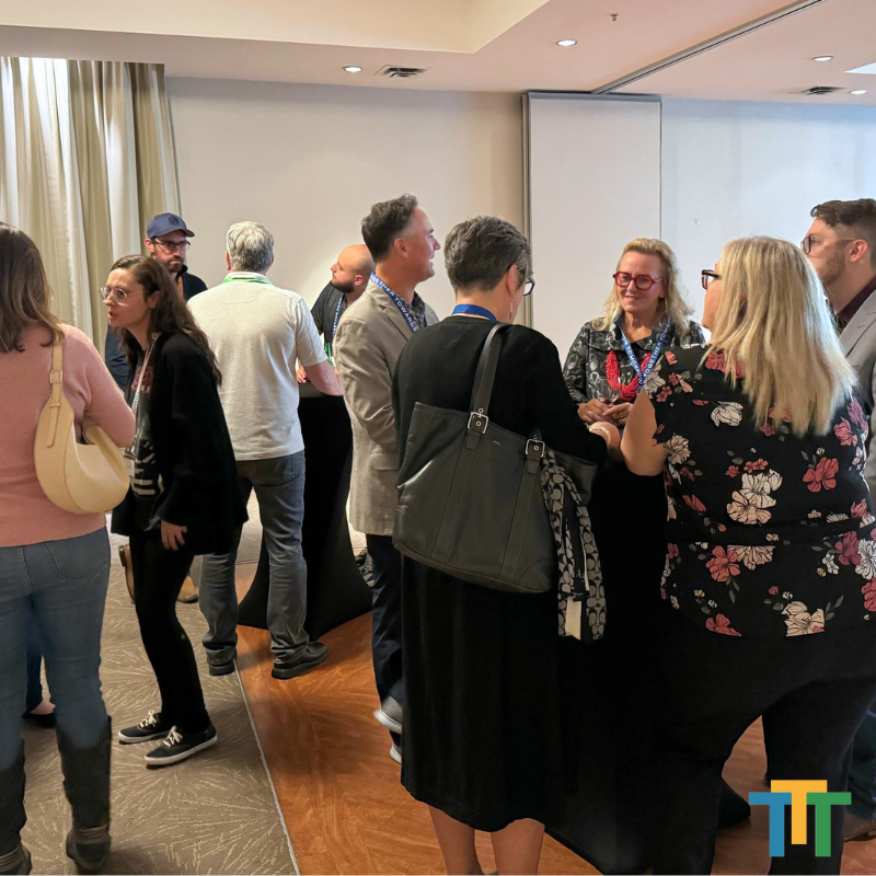 A group of people standing in a room with a t on the bottom right