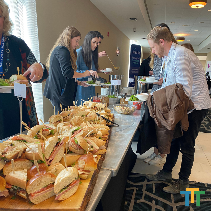 A group of people are standing around a table filled with sandwiches.
