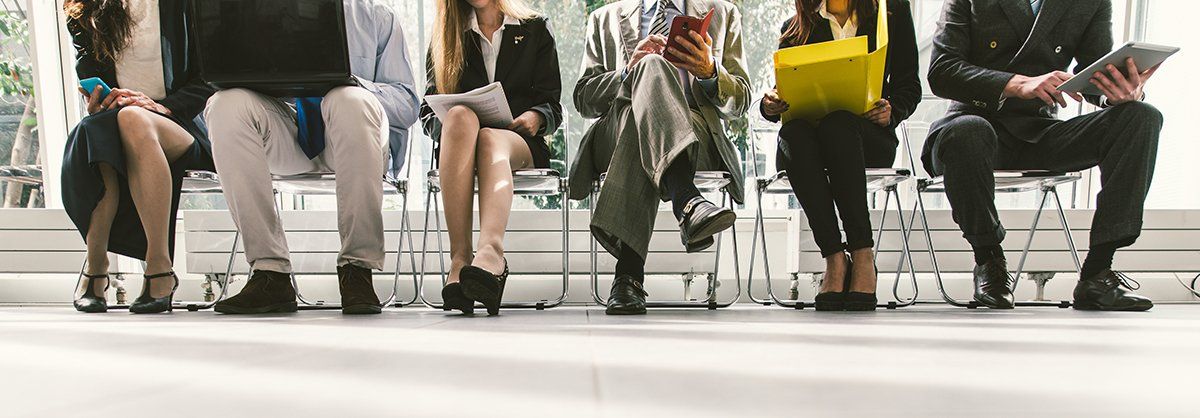 A group of people are sitting in a row waiting for a job interview.