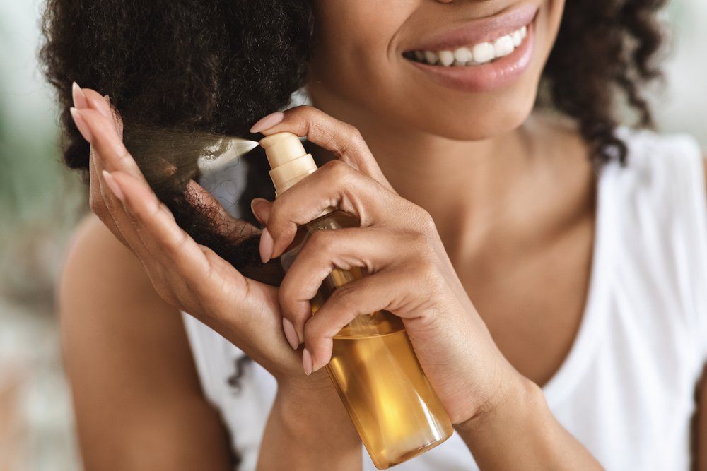 Une femme vaporise une bouteille d'huile sur ses cheveux.