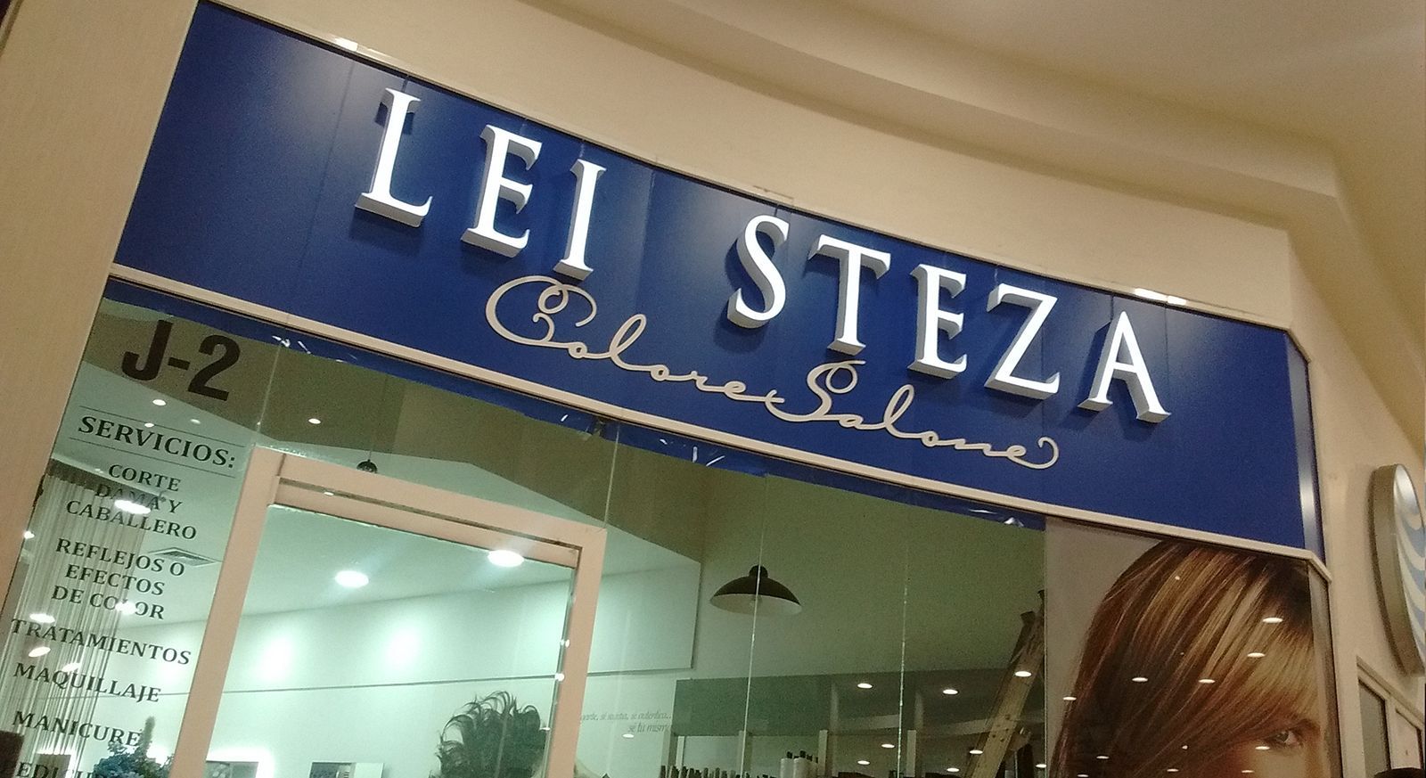 Cartel de Lei Steza Color & Salons, fondo azul, letras blancas y escaparate.