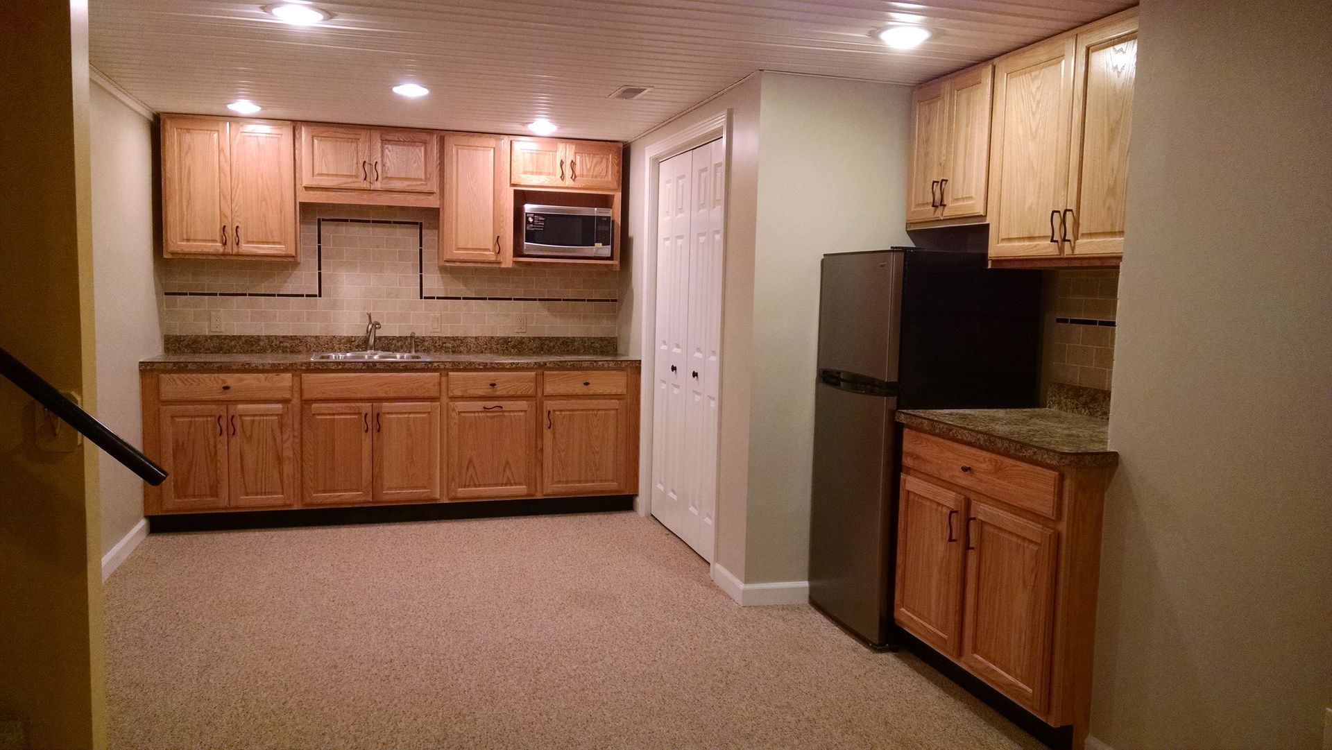 A kitchen in a basement with wooden cabinets and a refrigerator.