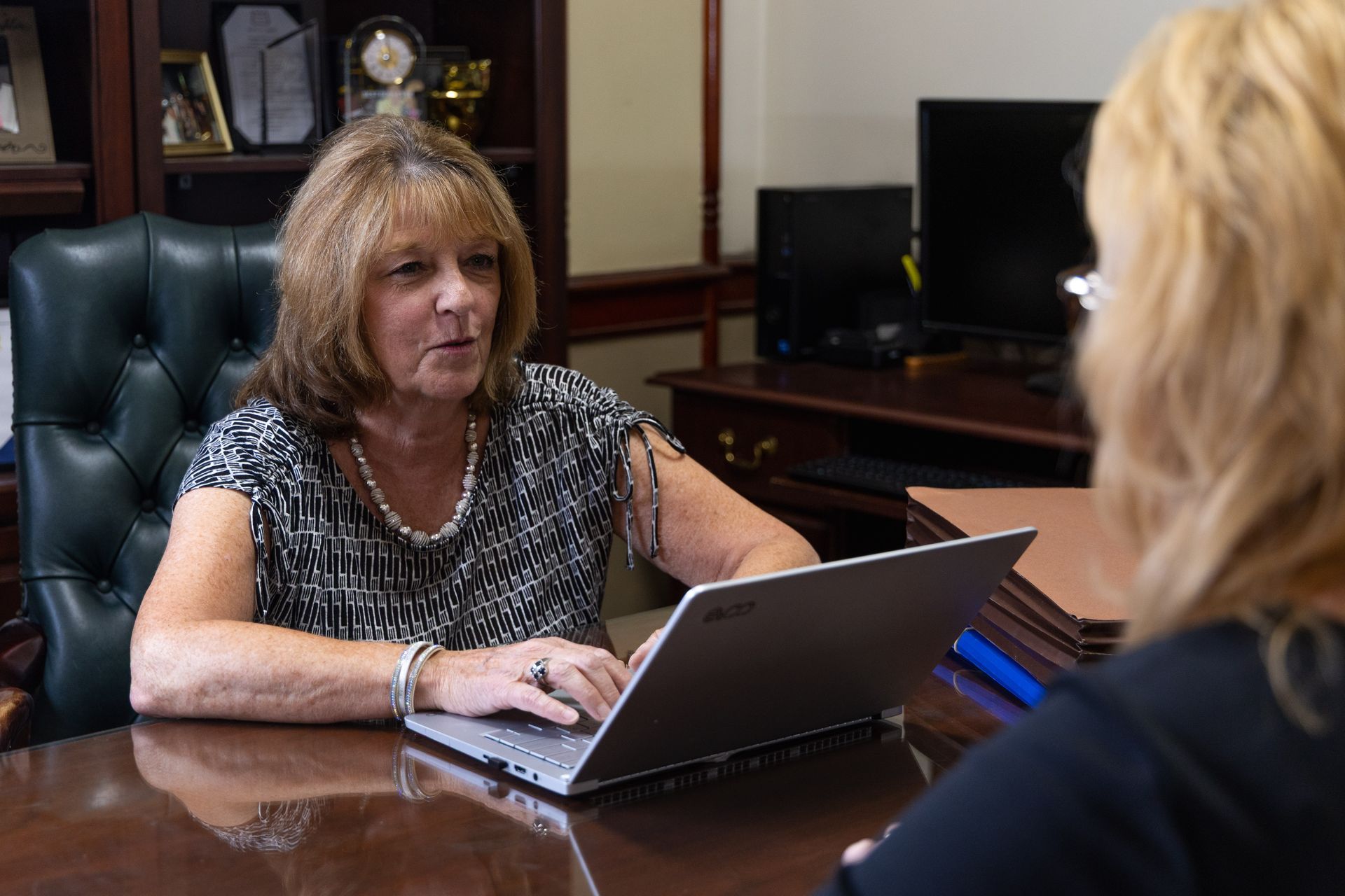 Two people in business attire discuss documents at a conference table in a wood-paneled office.