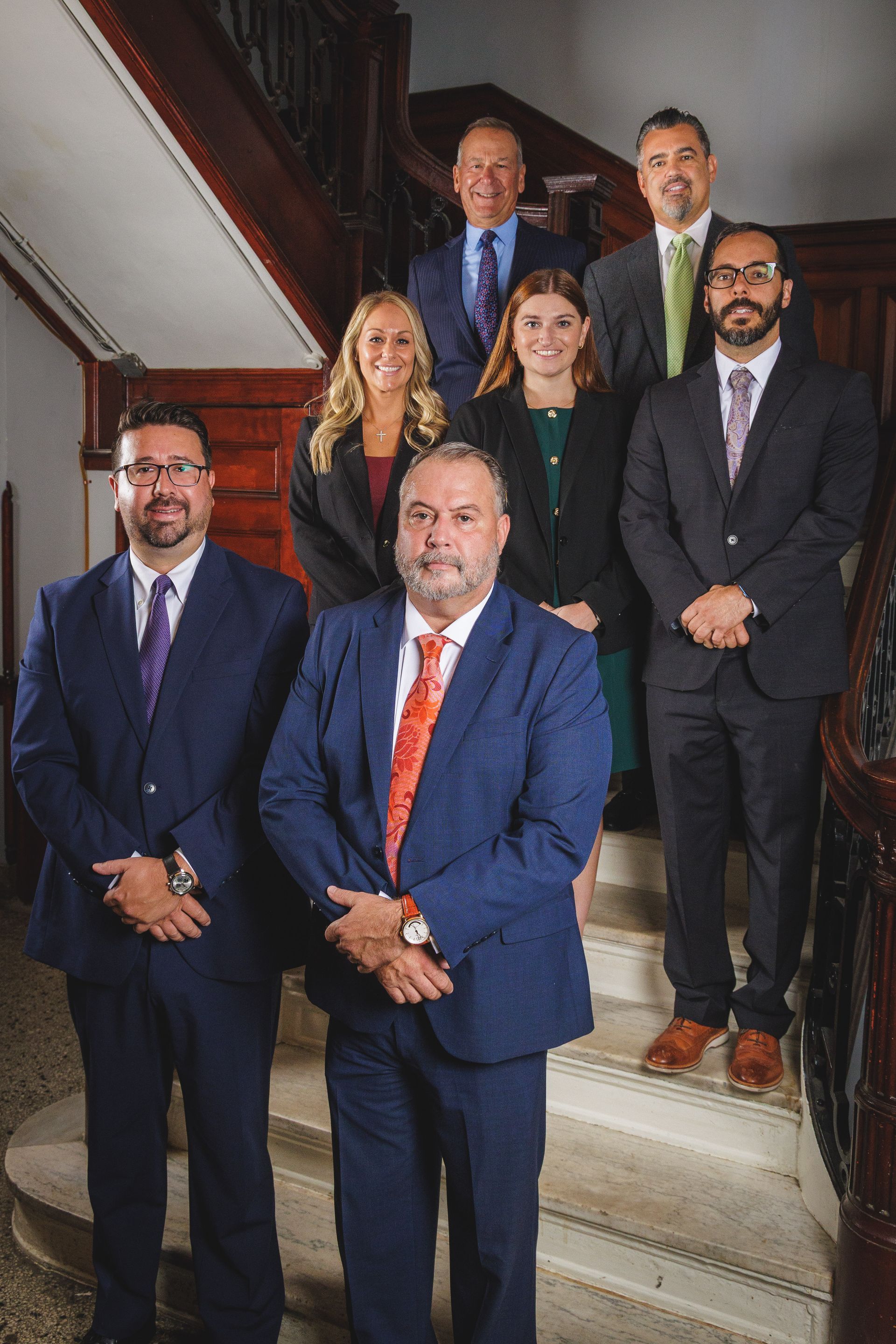 Group of people in formal attire posing on a staircase, looking at the camera.