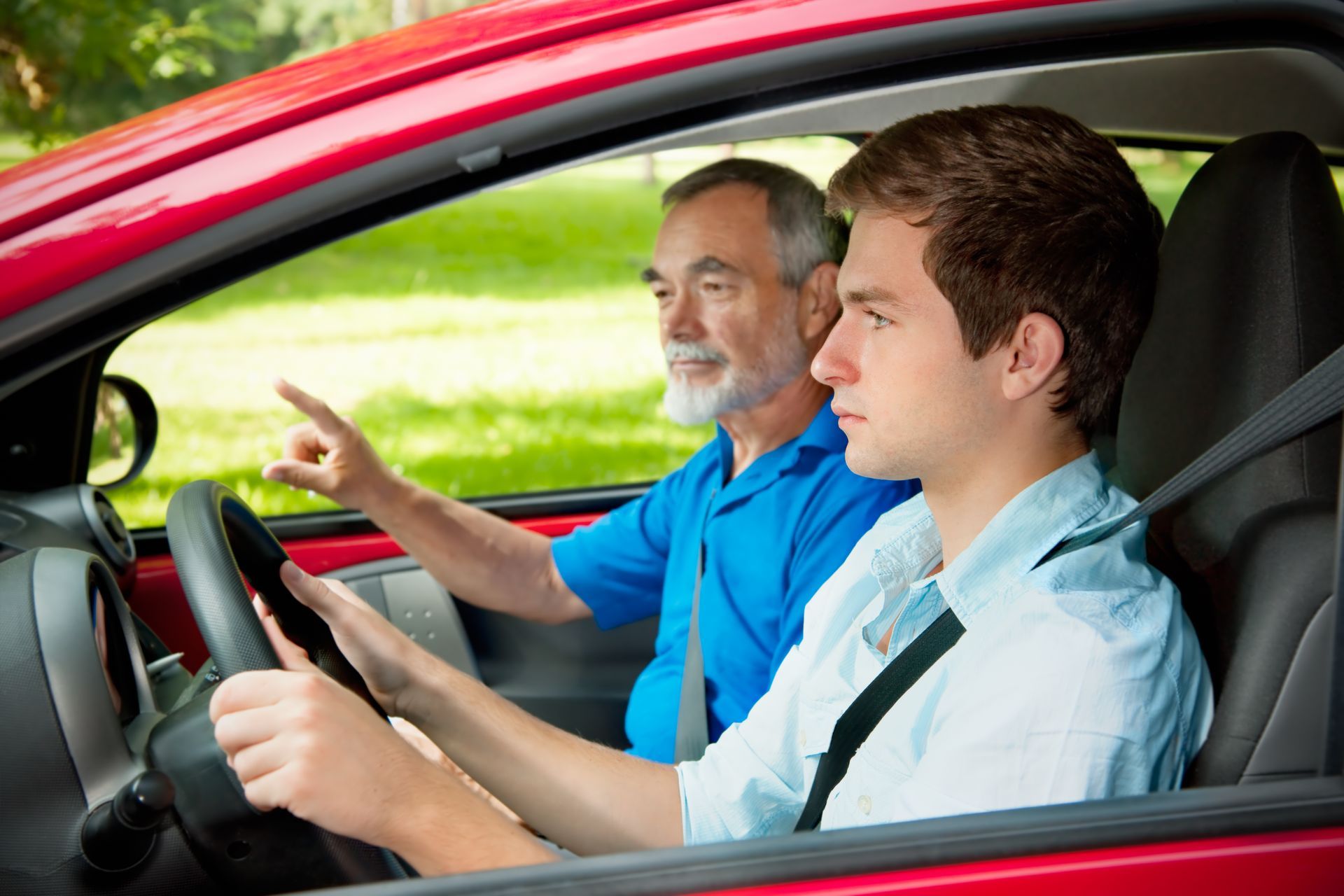 Man teaches teen to drive in red car; instructor points.