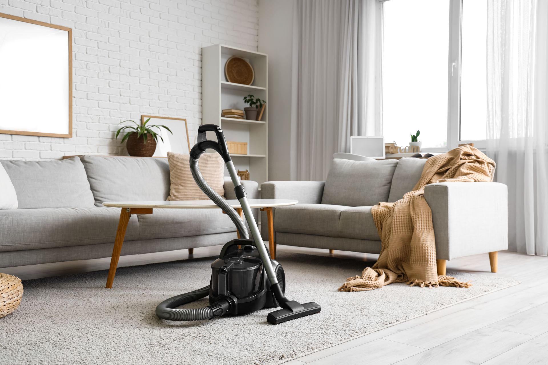 Living room with gray sofa, vacuum cleaner, and tan coat draped over a white chair