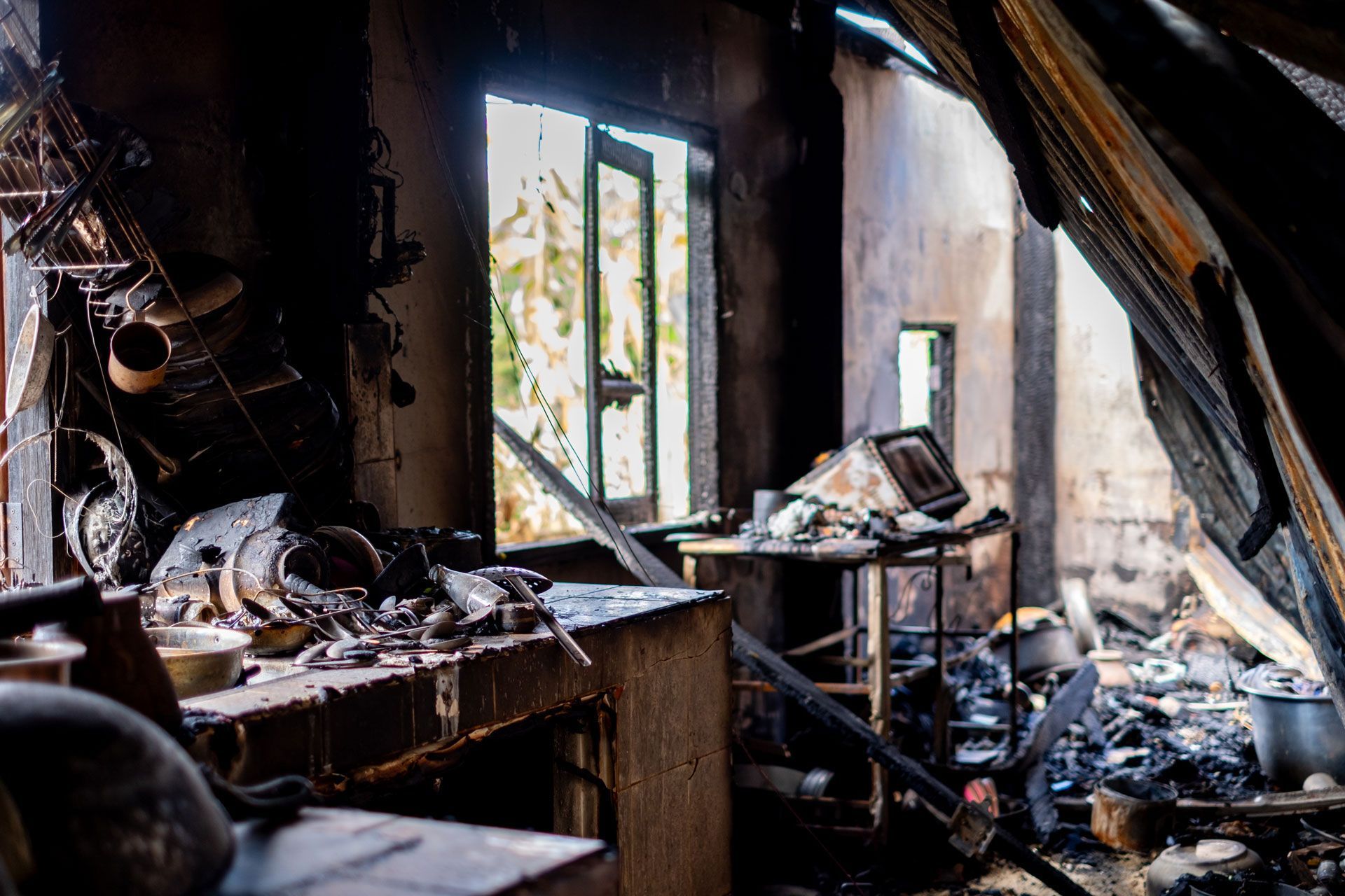 Burned, wrecked room with charred furniture and debris, light streaming through a damaged window