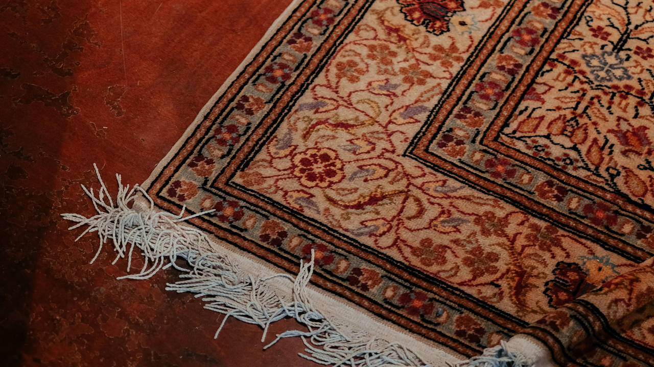 Beige and brown patterned rug with fringe on a red surface.