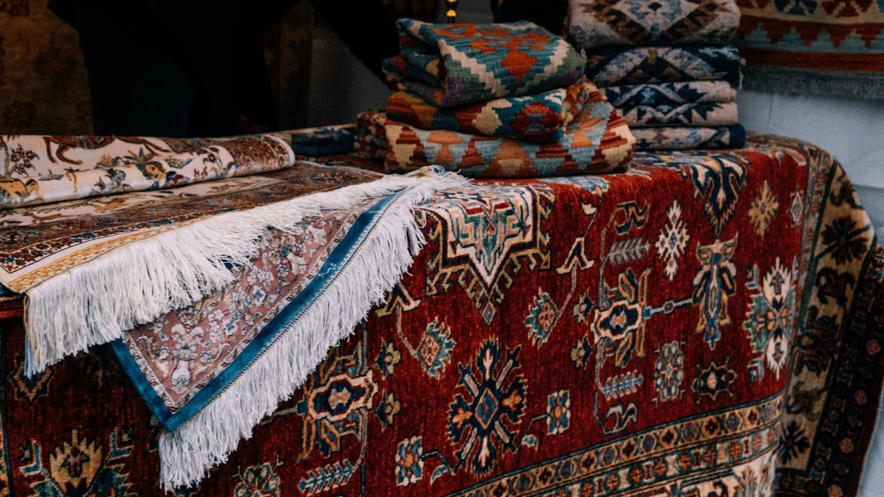 Display of colorful patterned rugs and carpets, some folded, on a table.