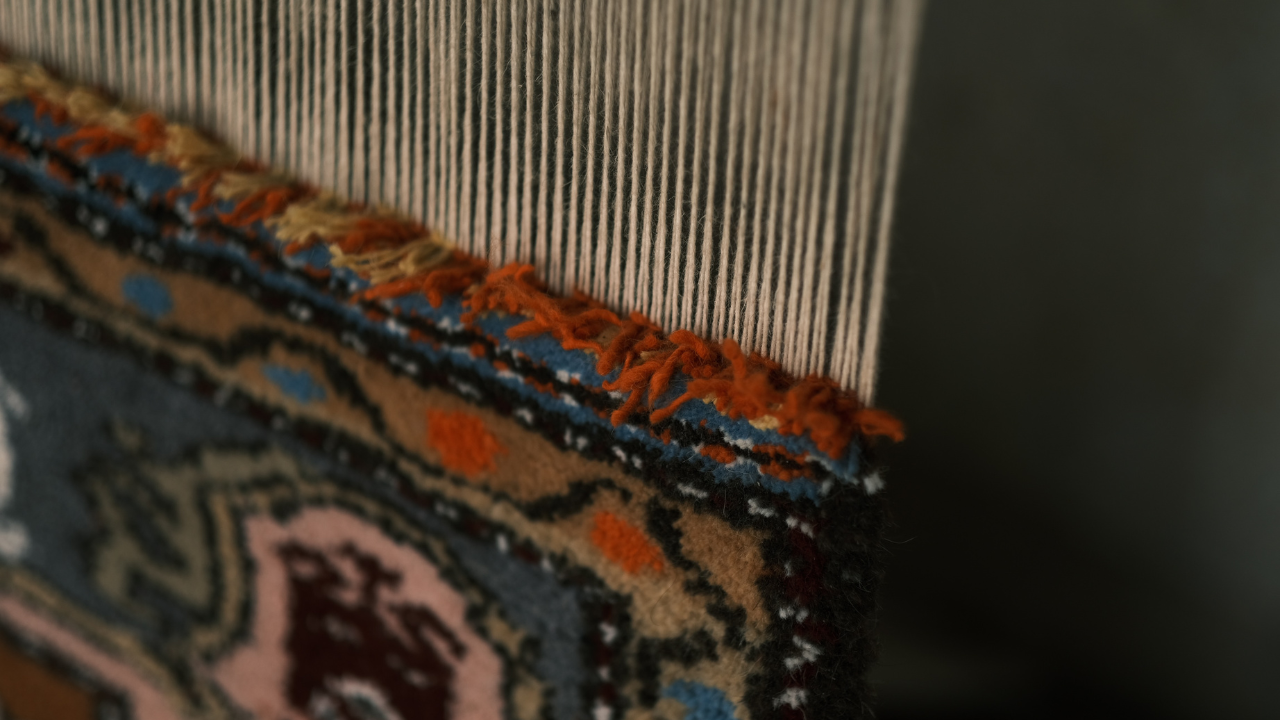 Close-up of a rug being woven on a loom, showing intricate patterns and colorful threads.