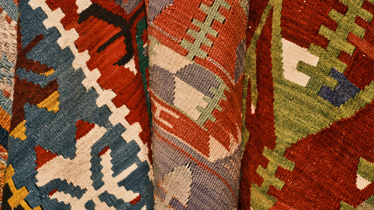 Close-up of rolled up colorful kilim rugs with geometric patterns in red, blue, green, and beige.