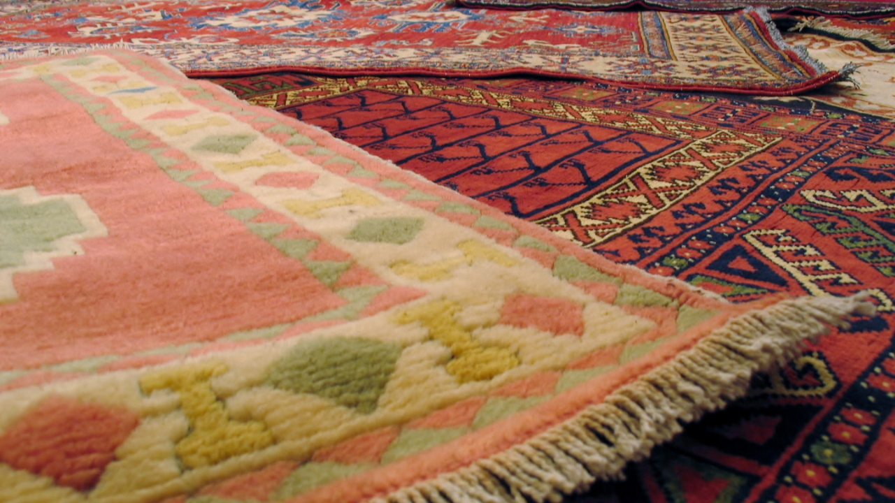 Close-up of several colorful oriental rugs piled together, showing intricate patterns and fringes.