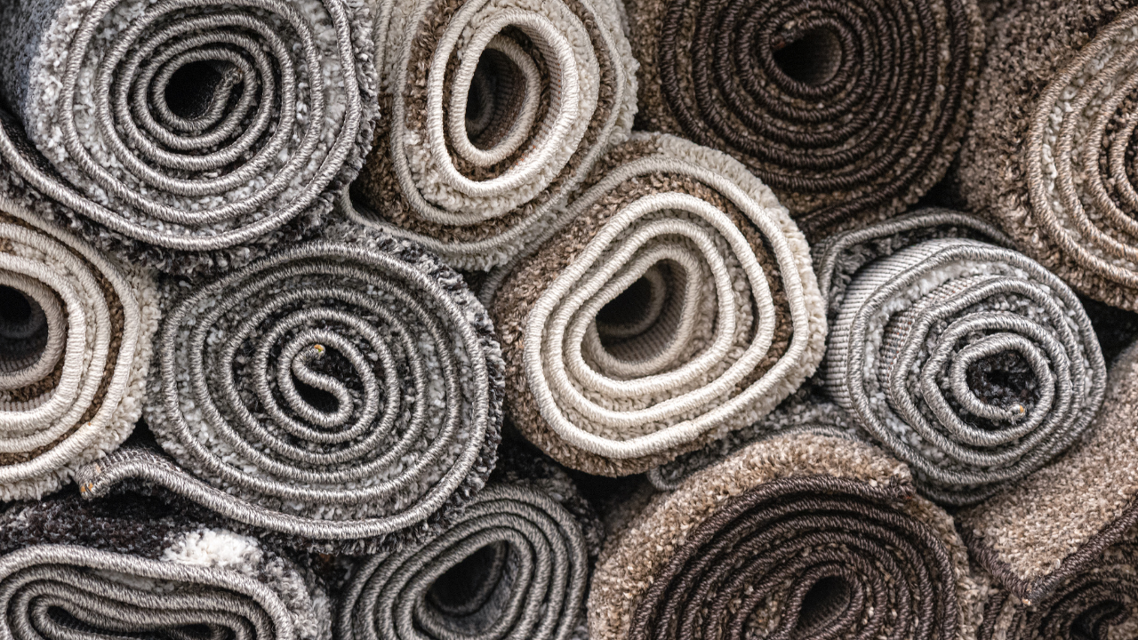Rolled up carpet rolls in various shades of gray and brown, stacked close together.