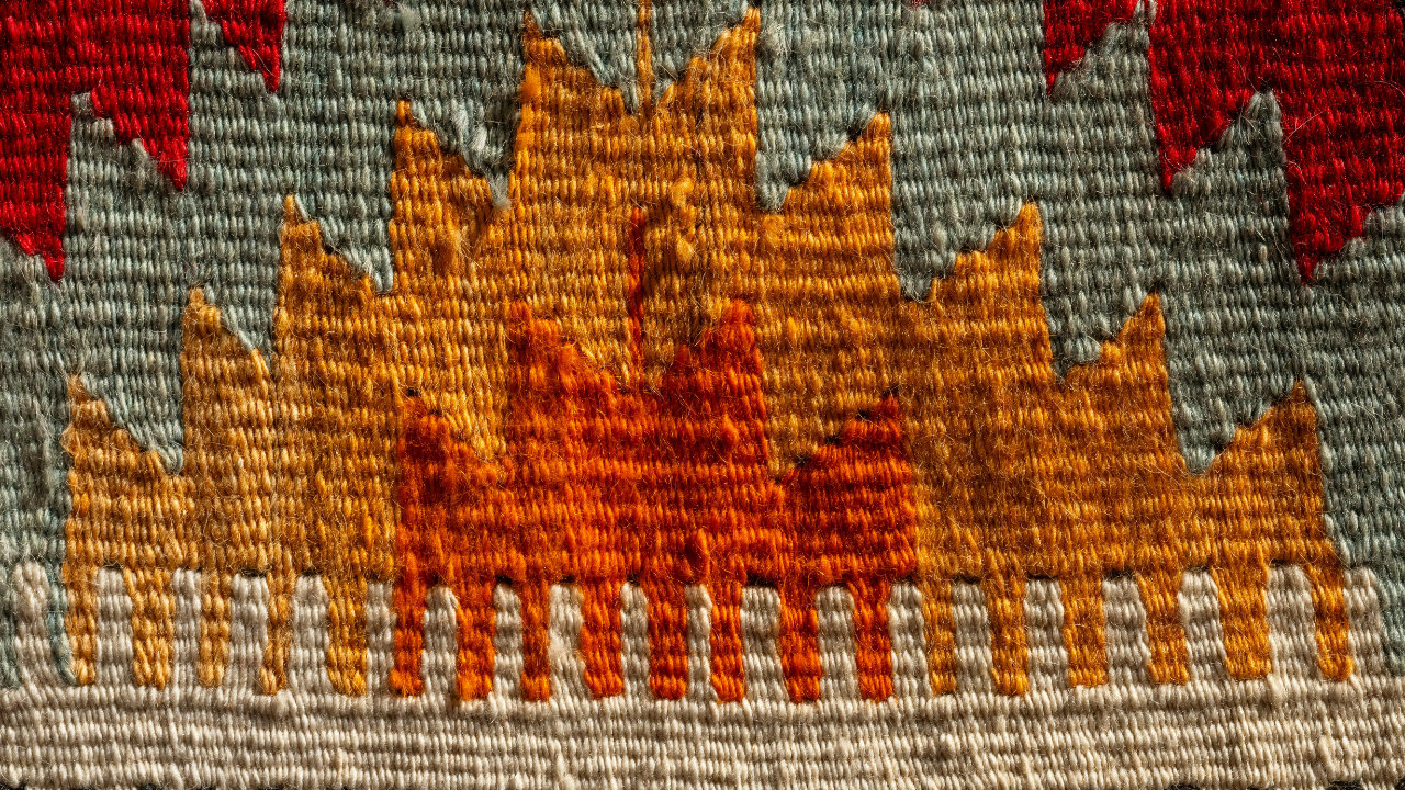 Close-up of a woven textile with a geometric flame pattern in orange, yellow, and red on a grey background.