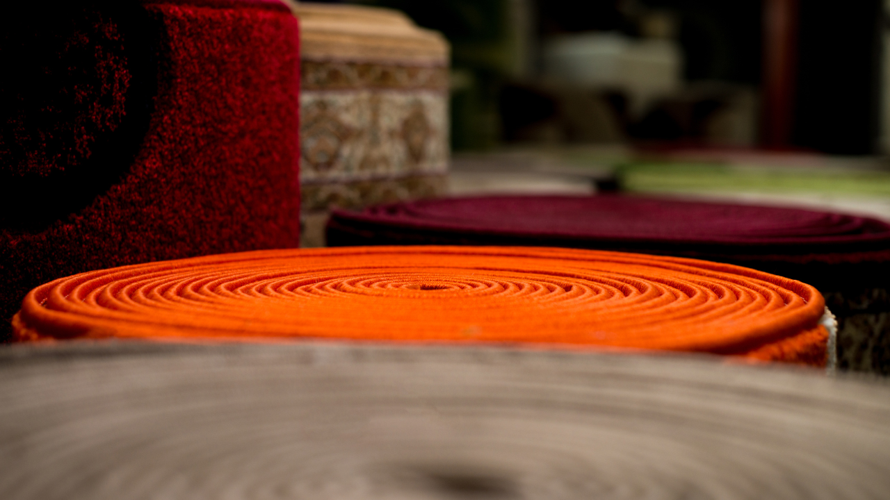 Orange, maroon, and patterned fabric rolls arranged on a wooden surface.