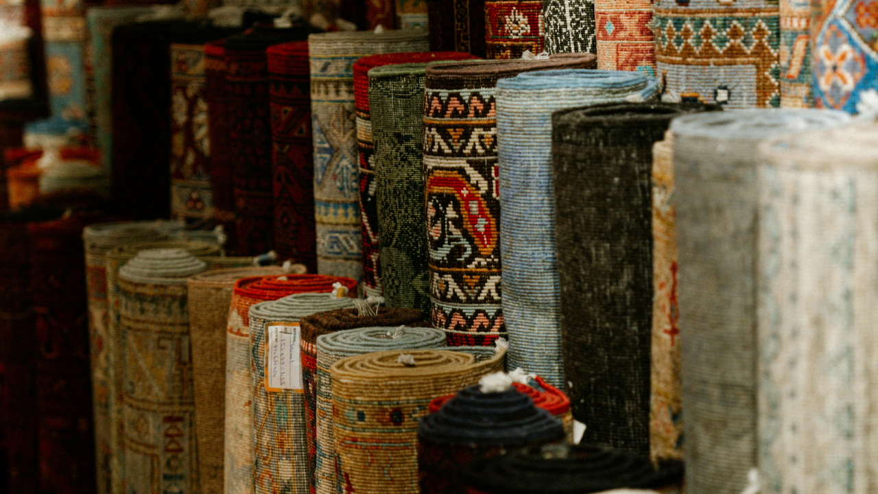 Rolled carpets of various colors and patterns displayed in an outdoor market.