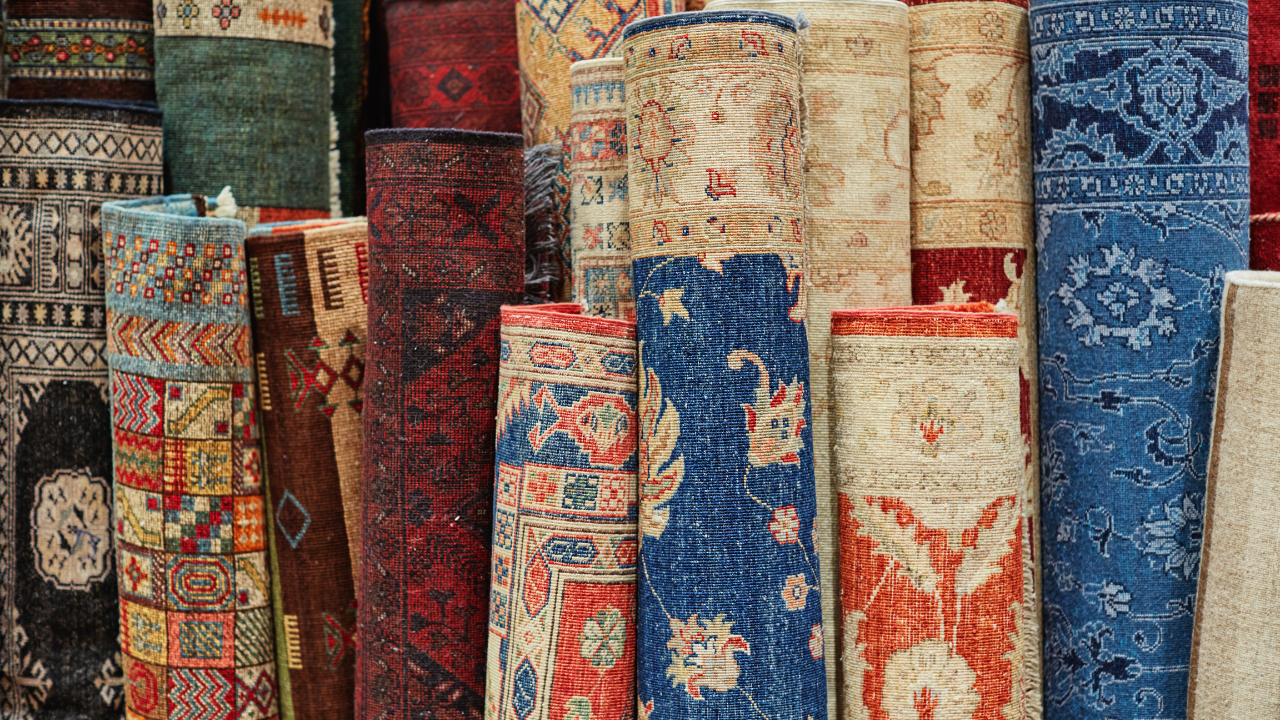Rolled rugs of various colors and patterns displayed in a shop, including blues, reds, and creams.