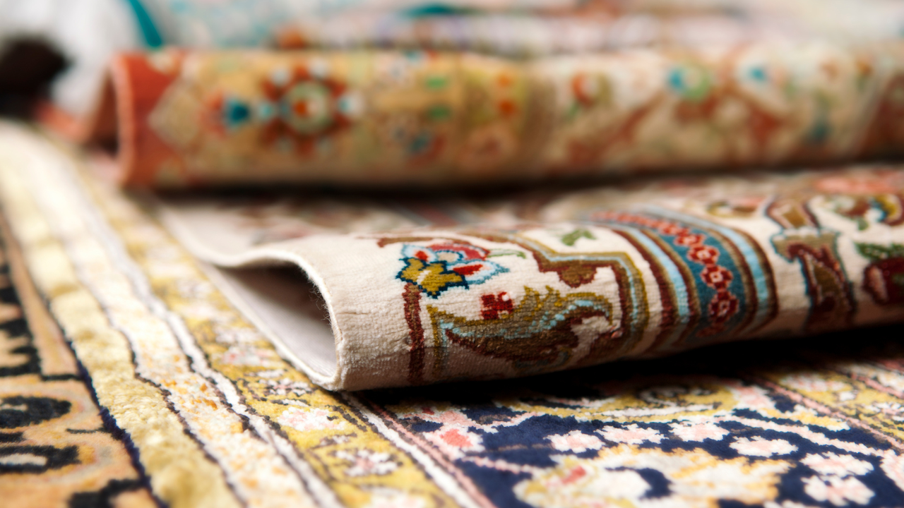 Rolled up patterned rugs, stacked, showing intricate designs and colors.