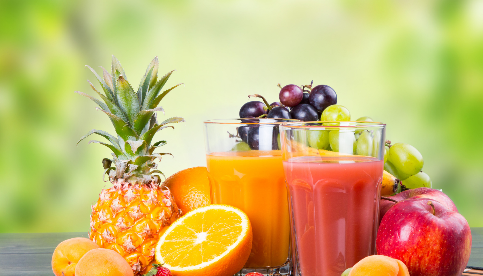 Assorted fresh fruits and juices on a table, including pineapple, oranges, grapes, apples, and red-orange drinks