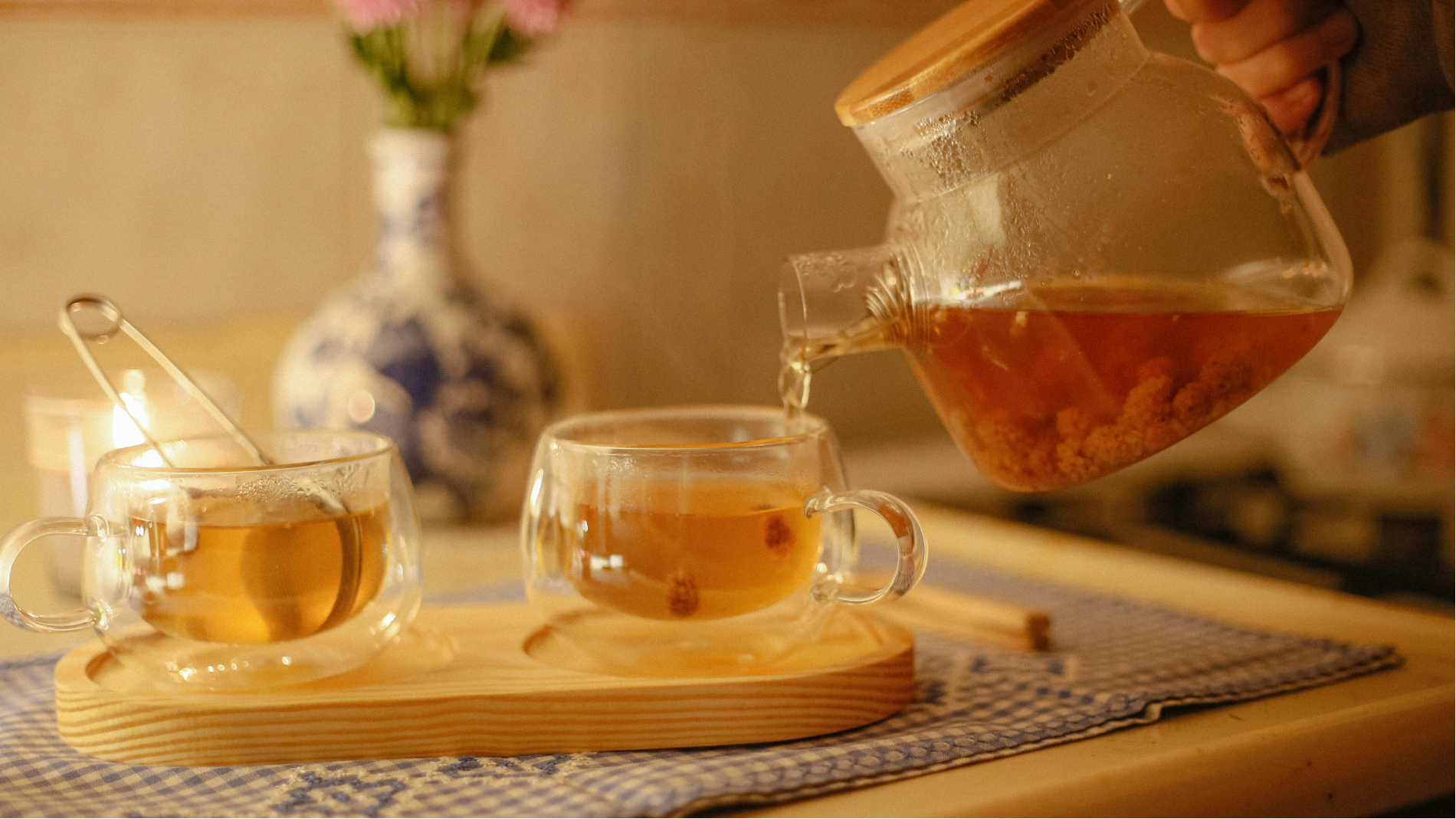 Tea being poured into clear cups on a tray in a warm, cozy kitchen setting