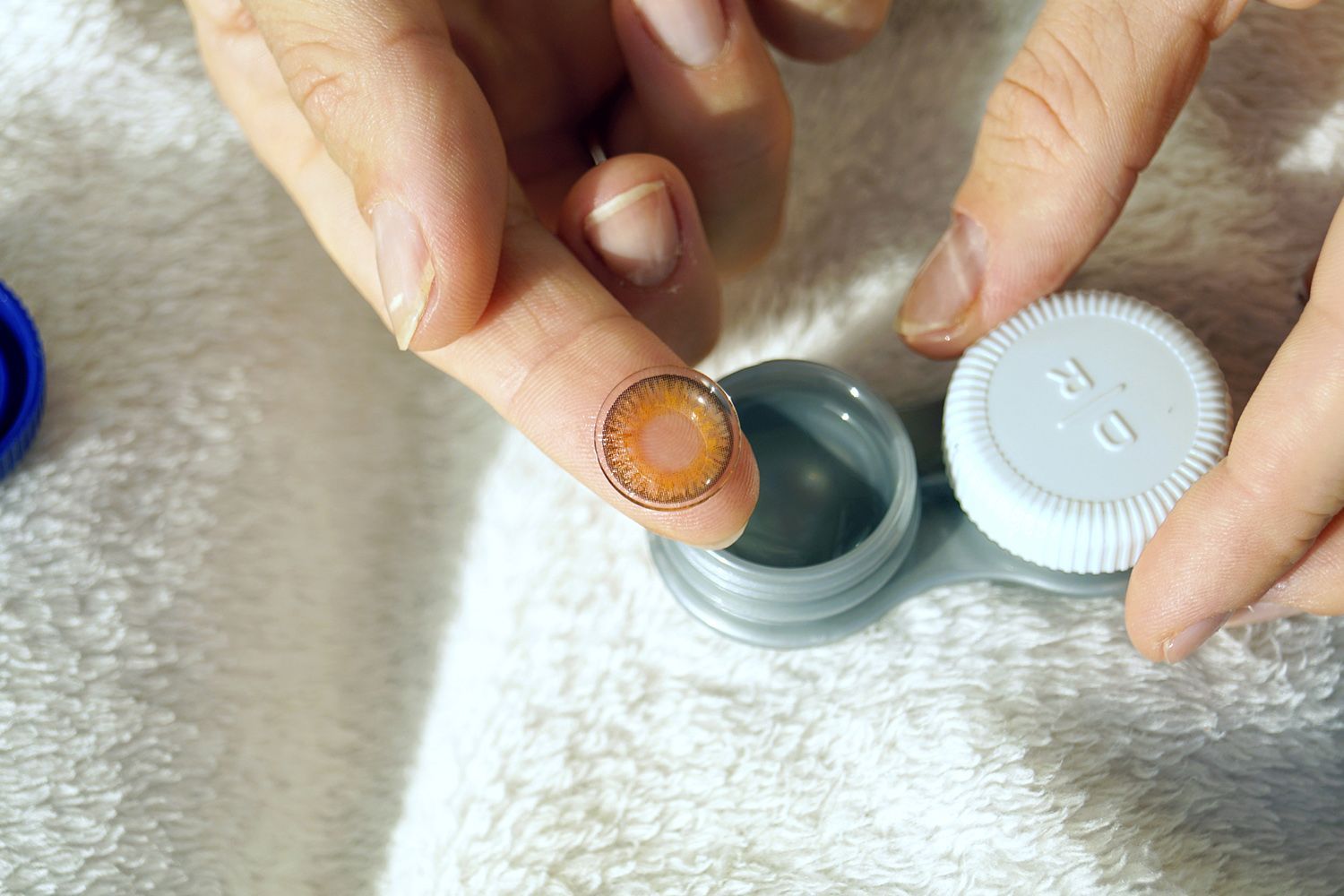 A person is putting a contact lens into a contact lens case.