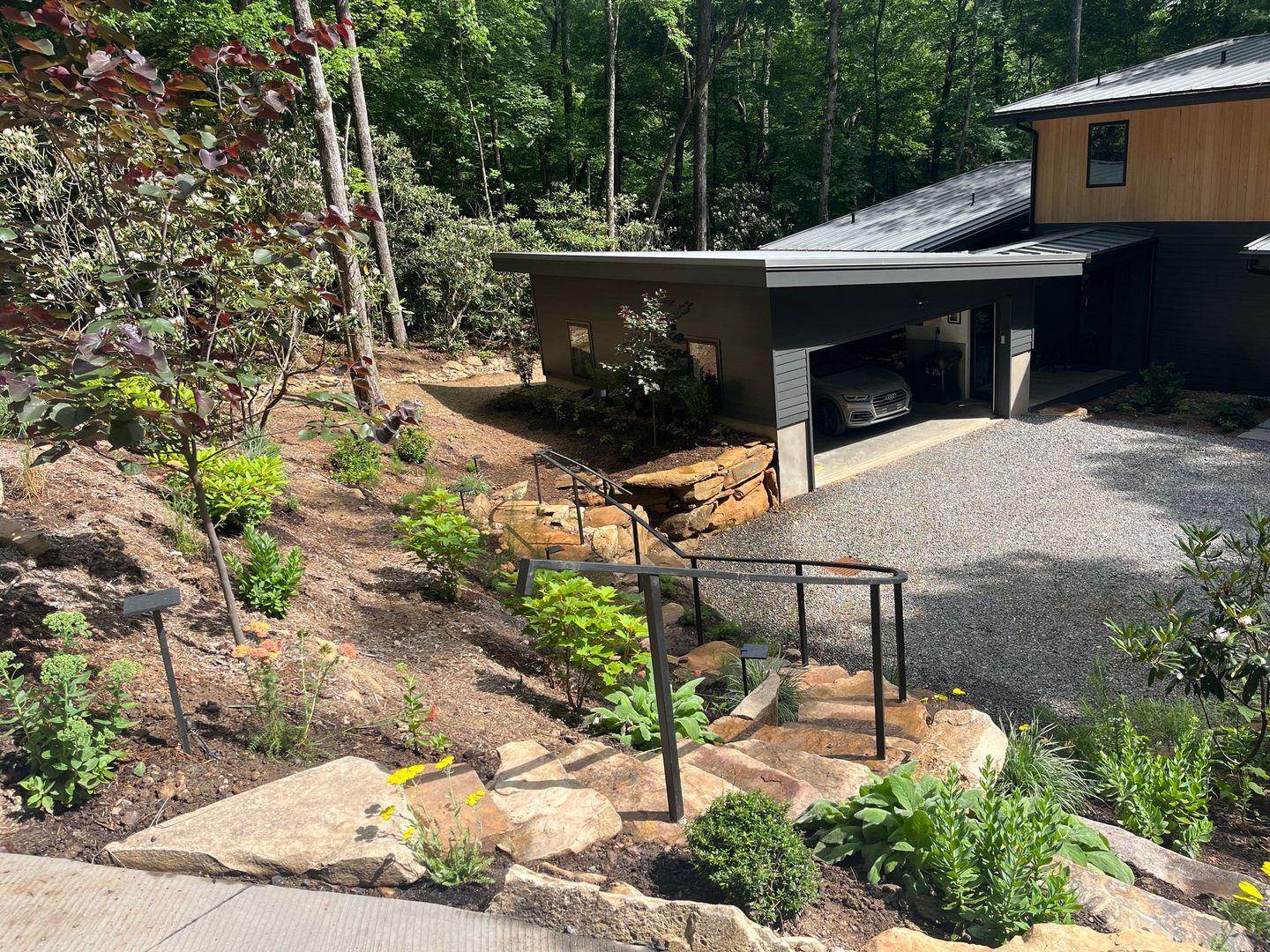 Landscaped backyard with stone steps, gravel driveway, and a carport beside a house.