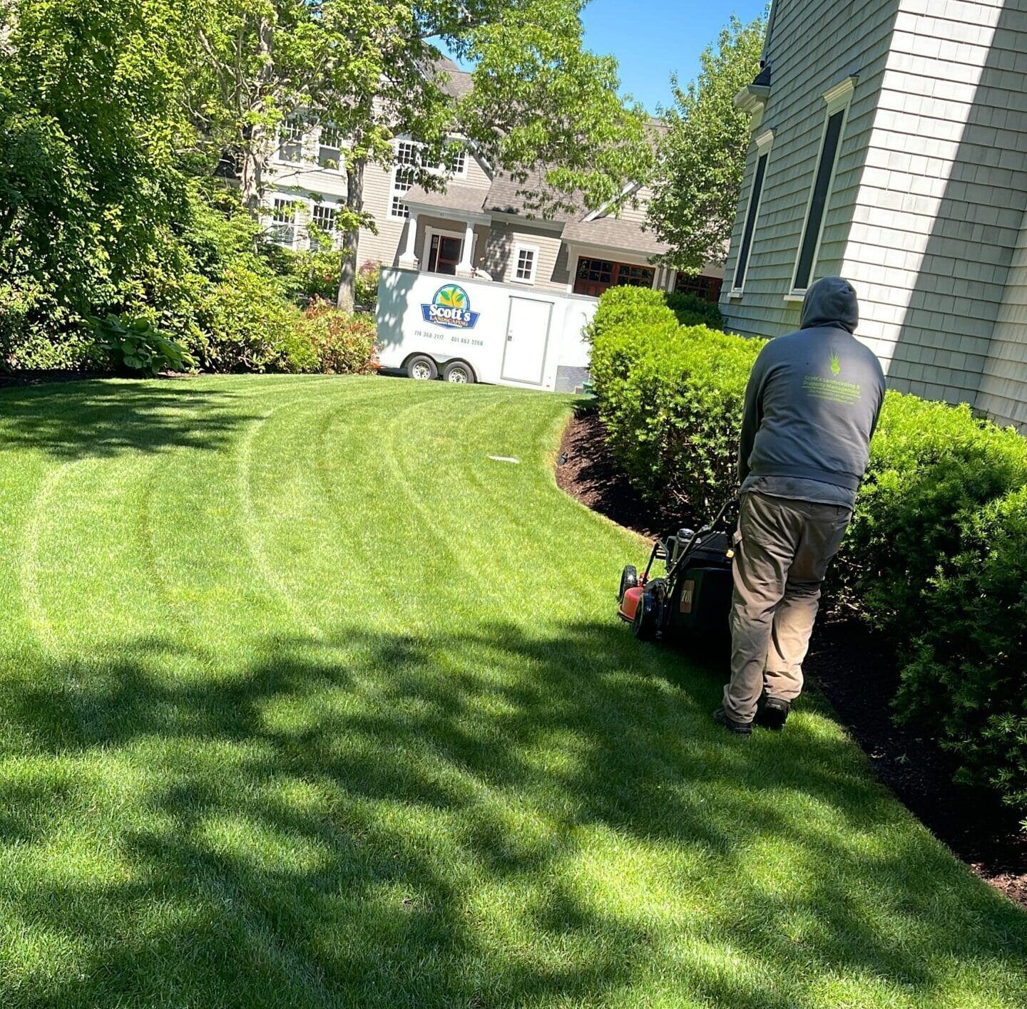 A man in a hat is cutting a bush with a pair of scissors.