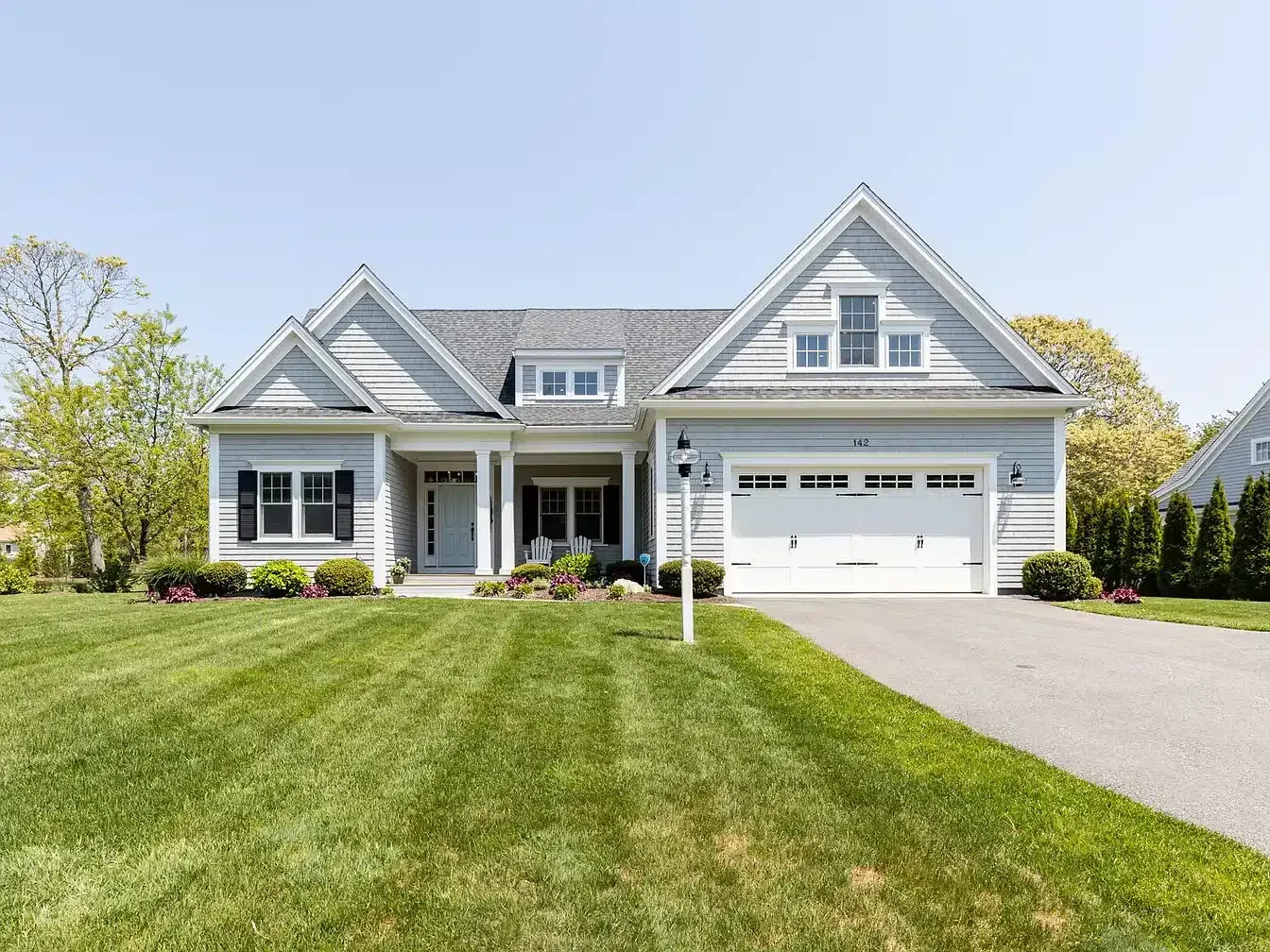 Gray suburban house with white trim, front lawn, and attached garage on a sunny day