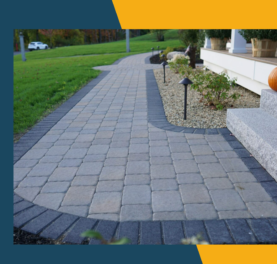 Curved gray paver walkway beside a house with landscaped edging and small path lights.