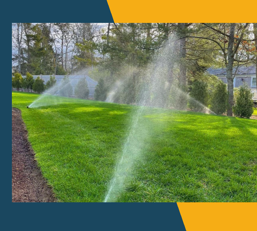 Lawn sprinklers watering a bright green yard beside trees and a house in autumn.
