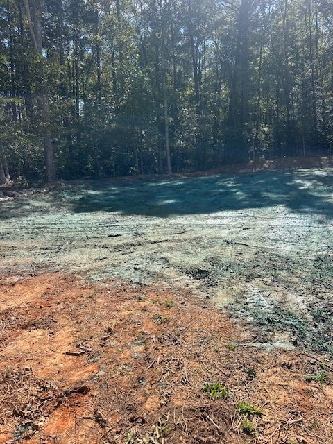 A construction site showing a patch of soil treated with green hydroseeding mulch bordering an area of bare red clay.