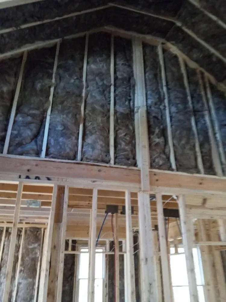 Interior view of a building under construction, showing wooden framing and insulation in the walls.