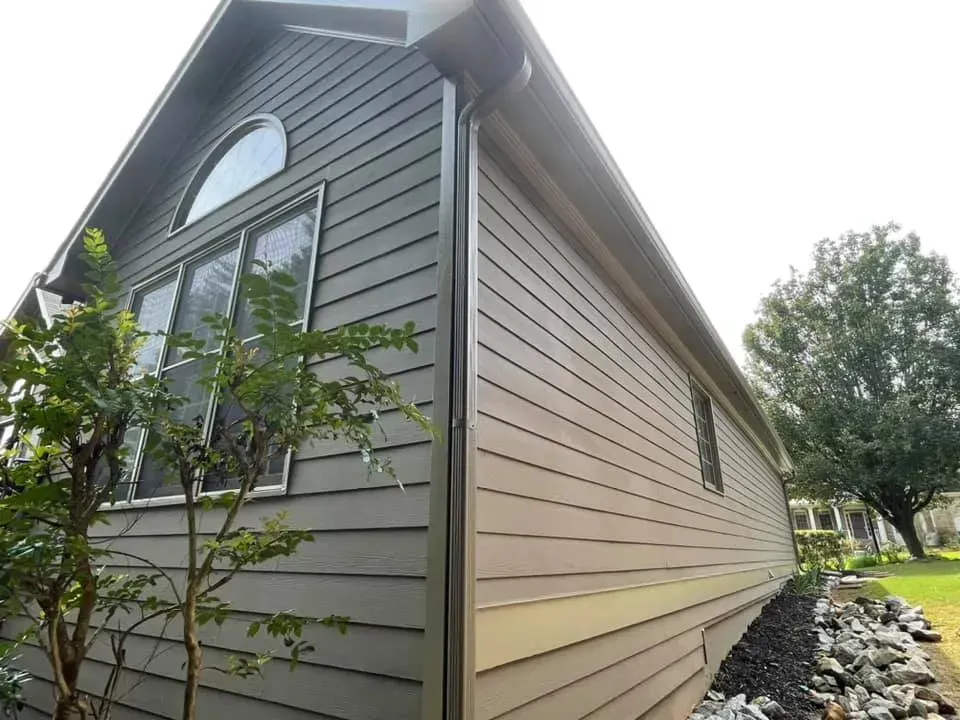 Gray house with horizontal siding and arched window, under a sunny sky.