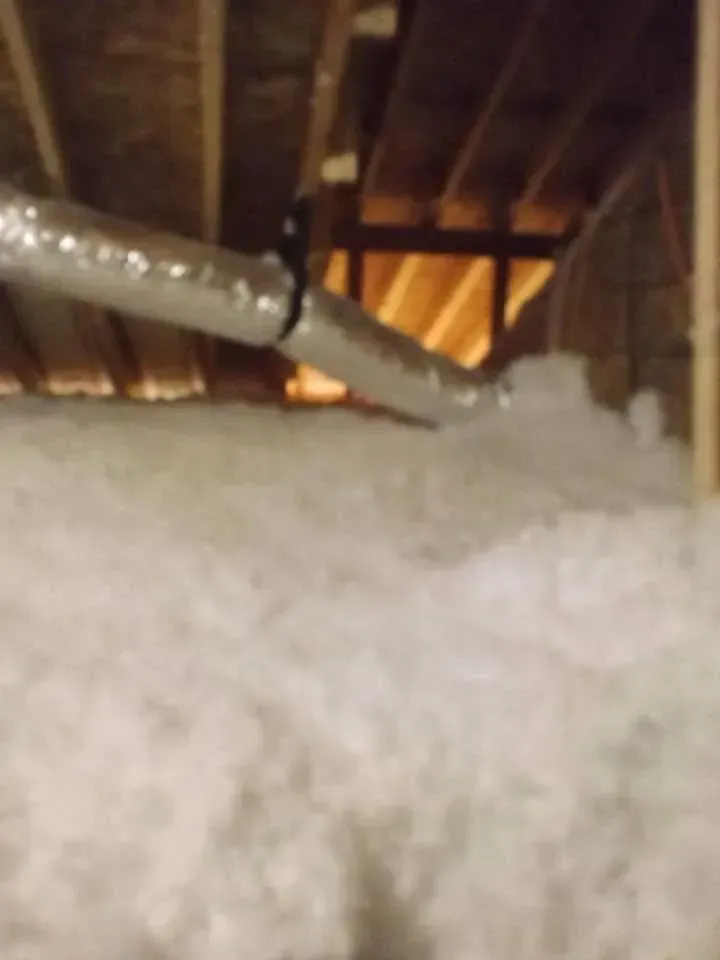 Attic space with silver ductwork and fluffy white insulation. Wooden beams and joists visible.