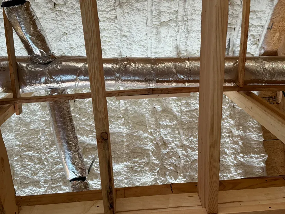 Attic space insulated with spray foam; ductwork visible. Wood beams and framing are present.