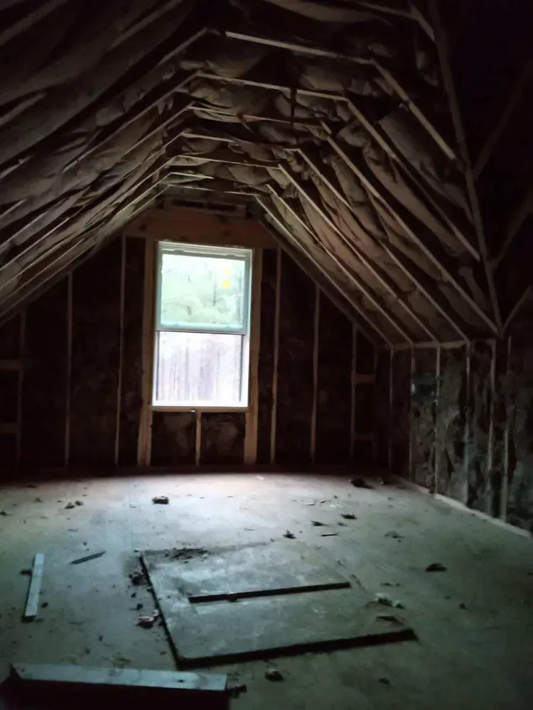 Interior of unfinished attic with a window and exposed wooden framing.