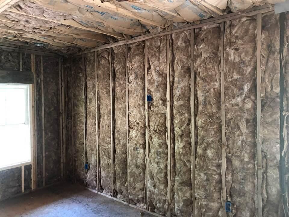 Interior view of a room under construction, showing wooden studs with insulation installed in the walls and ceiling.