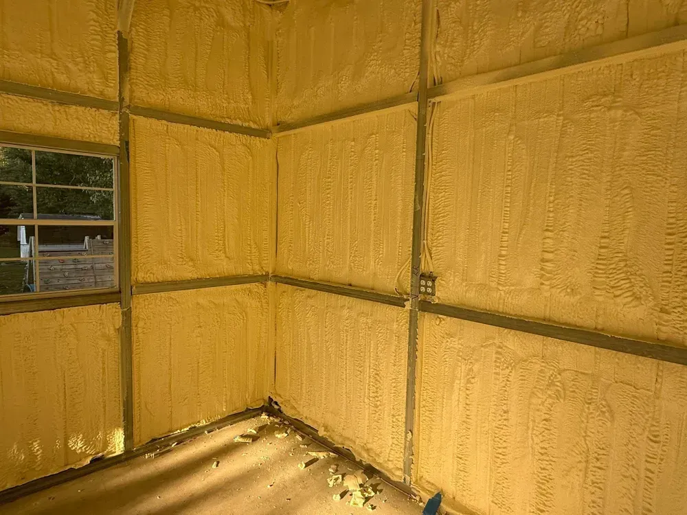 Interior view of a building with spray foam insulation on the walls. Window on the left, electrical box on the right.