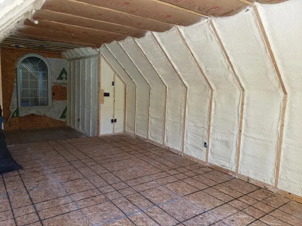 Attic interior with spray foam insulation on walls and ceiling, unfinished flooring.