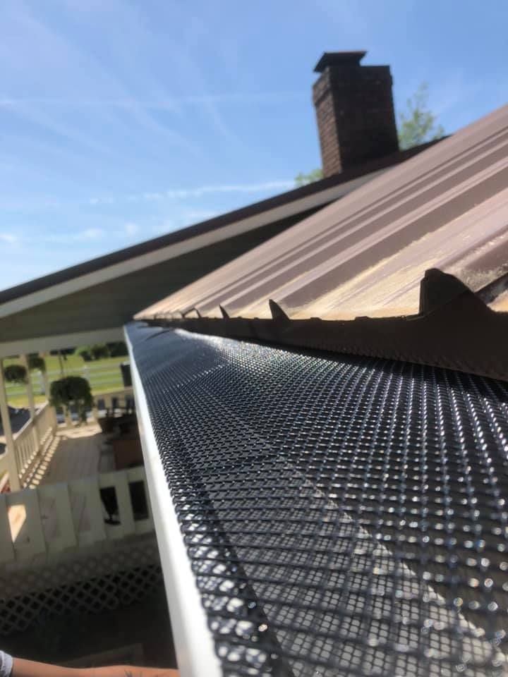 Gutter with black mesh guard on a roof, with a chimney in the background and a blue sky overhead.