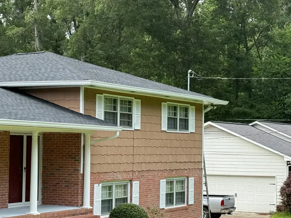 Tan house with brick accents, white trim, and a dark roof; a two-car garage sits beside it.