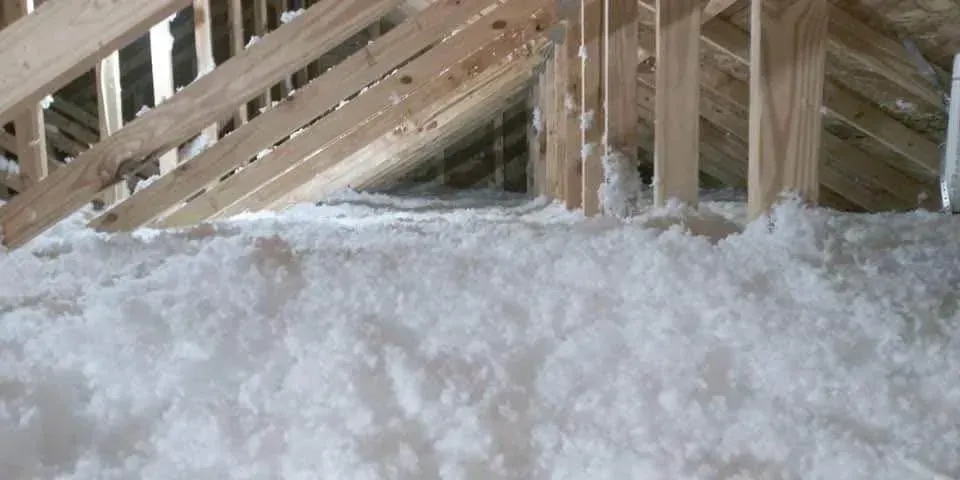Attic with wooden rafters and thick, white insulation covering the floor.