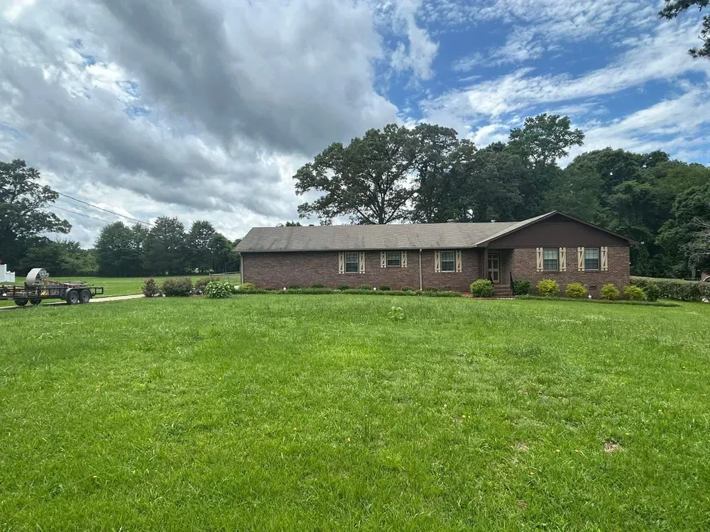 Brick ranch house with green lawn under a cloudy sky.
