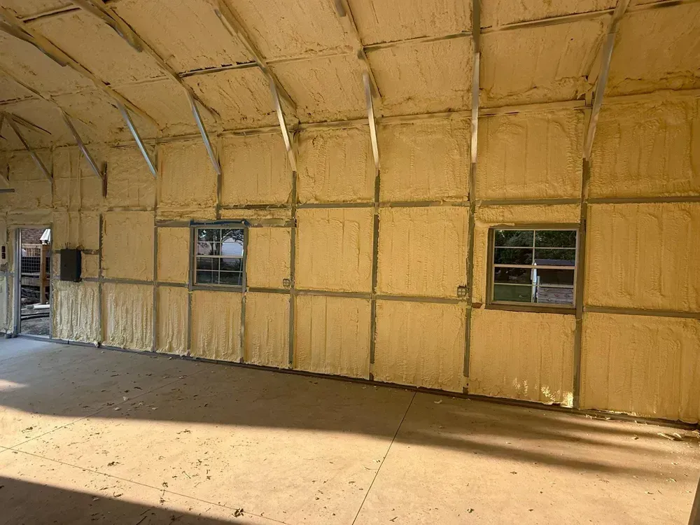 Person in protective suit spraying foam insulation into a wall frame in an indoor setting.
