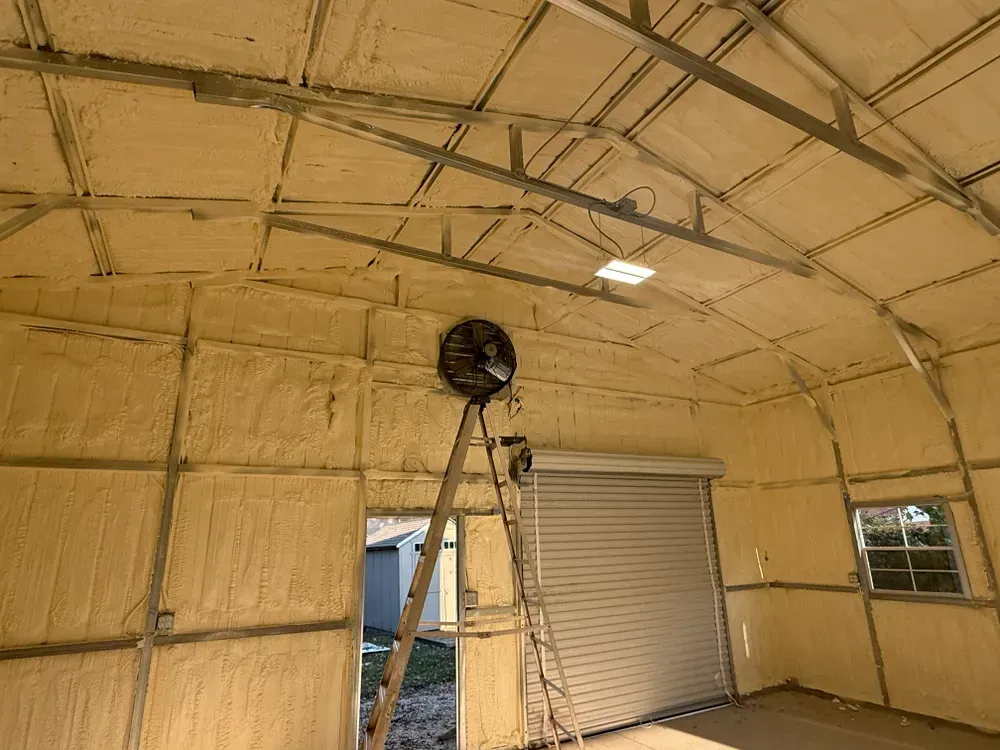 Interior of a building with foam insulation, including a fan, ladder, and a closed garage door.