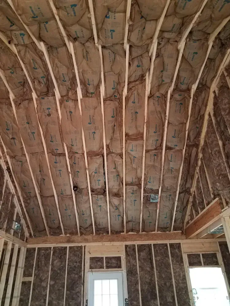 Interior view of wooden rafters with insulation installed in an unfinished house.