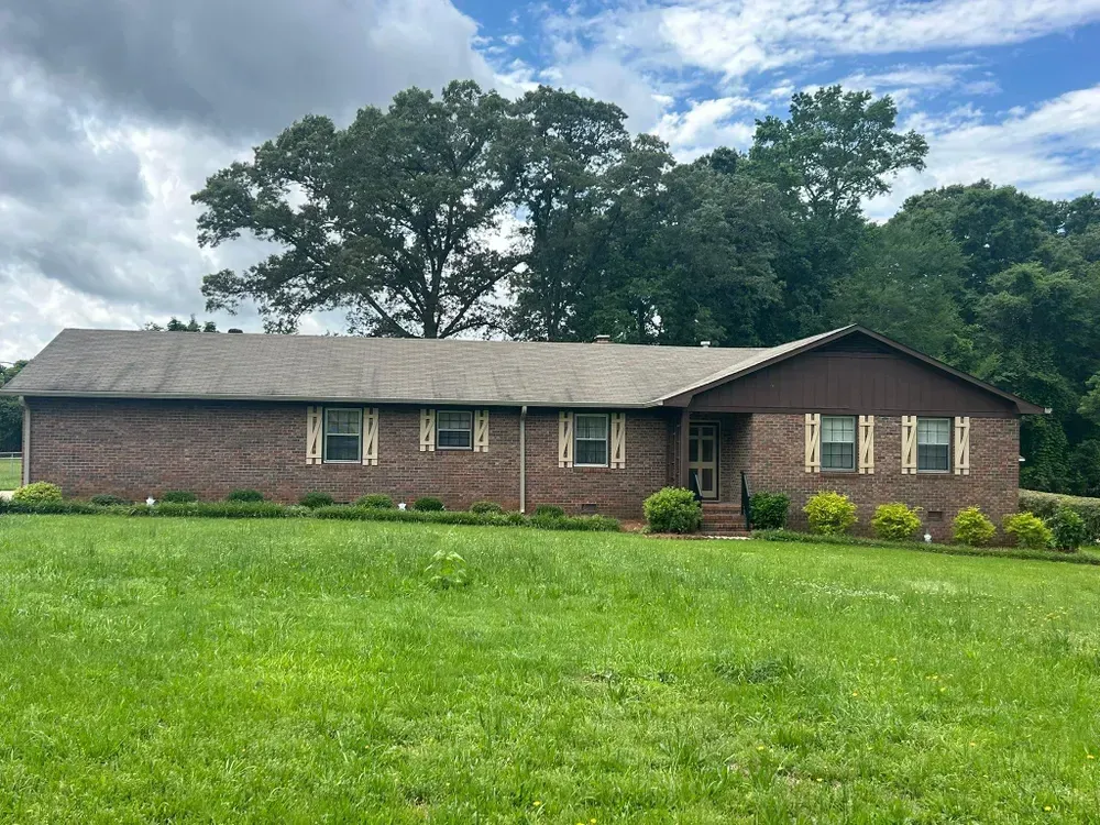 Brick ranch house with brown trim and shutters on a green lawn, under a cloudy sky.
