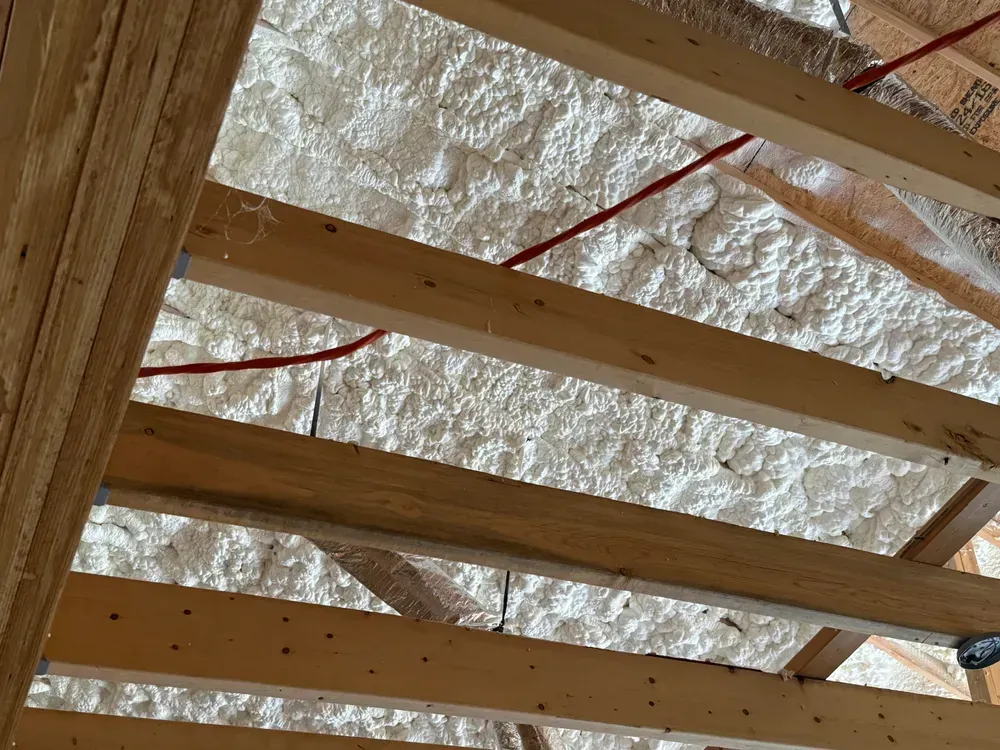 Wooden rafters with white foam insulation, red pipe. Construction setting.