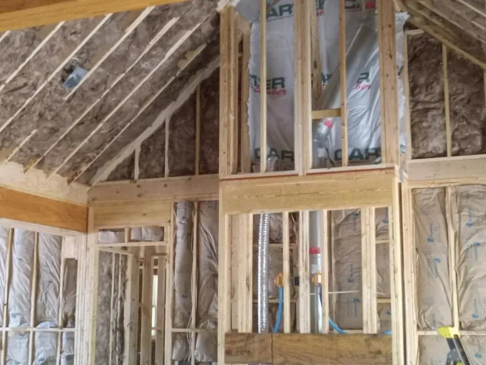 Interior view of a building under construction, showing wooden framing, insulation, and unfinished walls.