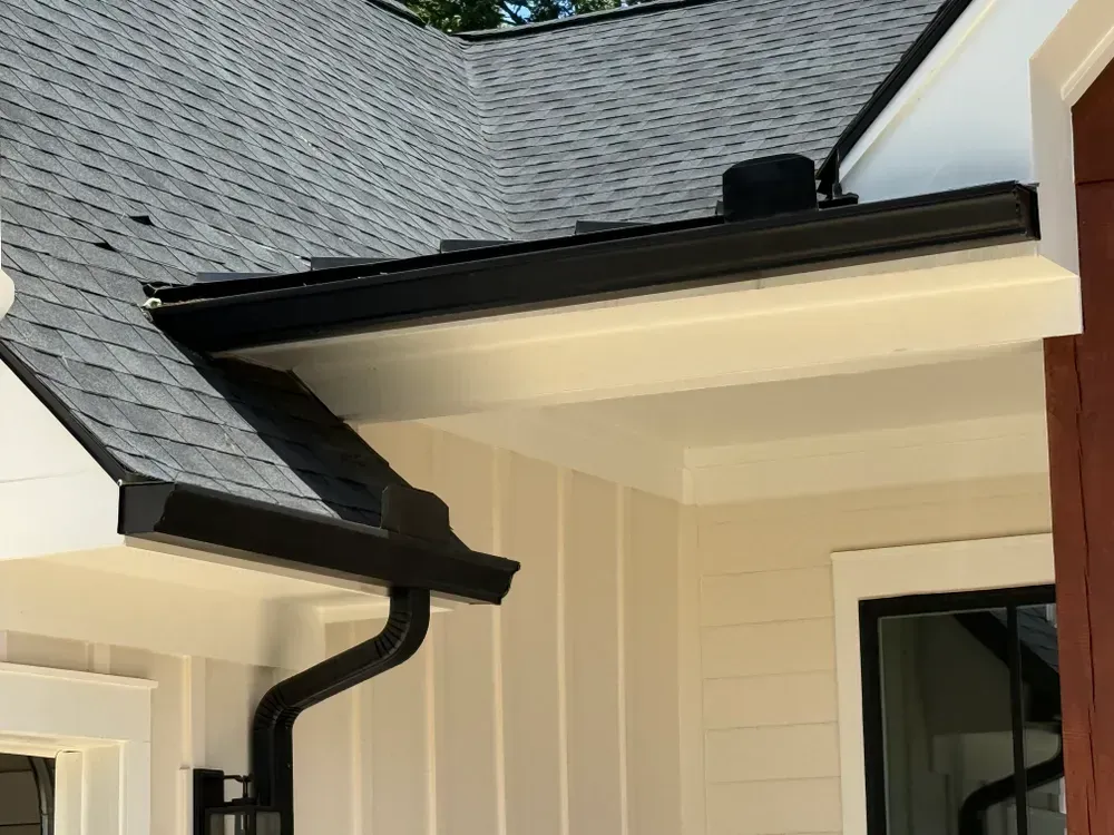 Black gutters on a building with shingle roof and off-white siding.
